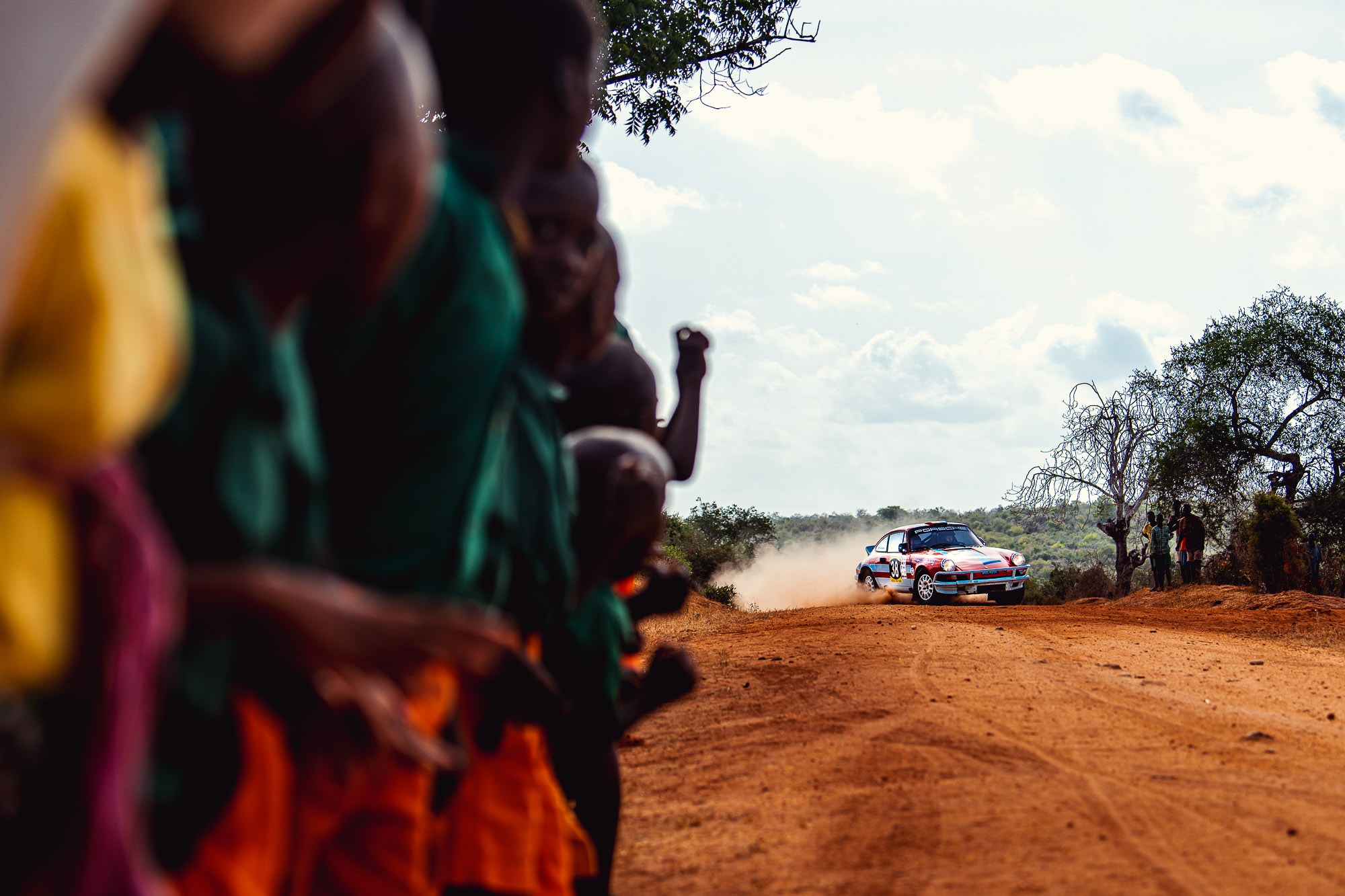 A Tuthill Porsche 911 goes around a corner in Kenya for the East African Safari Classic Rally as locals watch